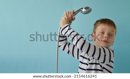 A happy smiling boy with a watering can from the shower over his head on a blue background. The concept of housewarming, renovation, happy childhood. Place fo text. Royalty-Free Stock Photo #2154616241