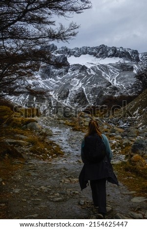 Back view of a caucasian woman walking on a mountain path with a snowy mountain in the background. Vertical. With copy space.