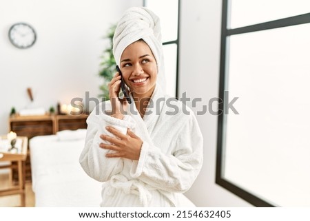 Young latin woman wearing bathrobe holding credit card at beauty center
