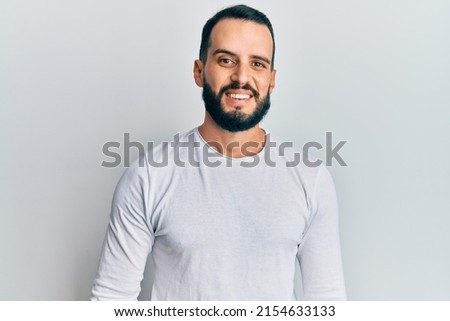 Young man with beard wearing casual white shirt with a happy and cool smile on face. lucky person. 
