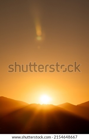 glints of the sun setting behind a mountain with a completely clear, orange sky at sunset Royalty-Free Stock Photo #2154648667