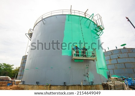 The male worker takes the cable car holding an industrial painting brush used for shell plate tank oil surface surface green color coating. Royalty-Free Stock Photo #2154649049