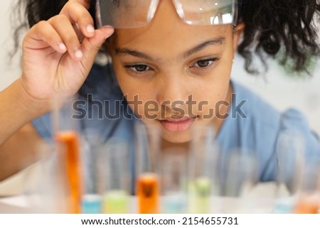 Close-up of biracial elementary schoolgirl looking at chemicals in test tubes during chemistry class. unaltered, education, learning, scientific experiment, stem, protection and school concept. Royalty-Free Stock Photo #2154655731