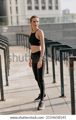 Full-lenght outdoor portrait of trendy stylish slim woman in sport outfit is preparing for sport training on sport square in sunlight . High quality photo