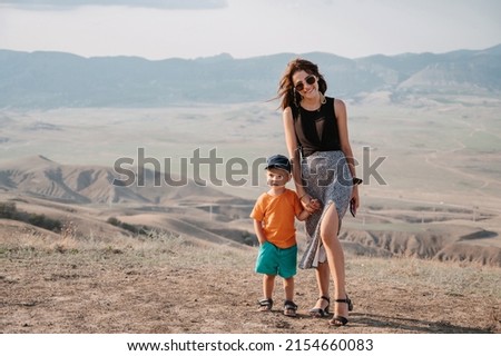 A young tourist with her young son climbed the mountains. A woman and a boy are standing at the top. Active recreation.