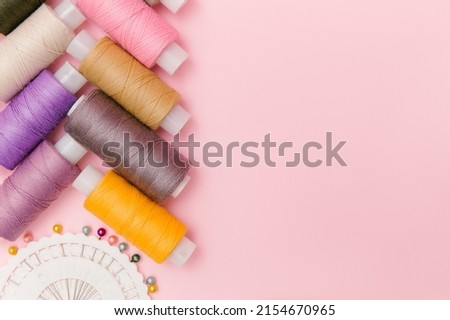 Sewing tools and sewing accessories on elegant pink background. Dressmaking, tailor background. Multicolor sewing threads, thread spools, needles, pins. Top view, flat lay for tailor's business. Royalty-Free Stock Photo #2154670965
