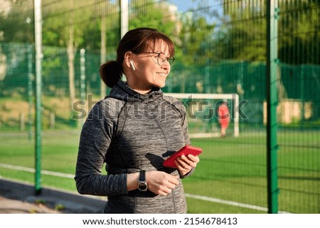 Active mature woman in sportswear headphones with smartphone, outdoor