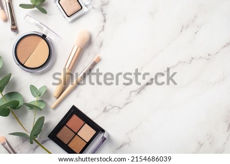 Make-up concept. Top view photo of makeup brushes contouring eyeshadow palettes and eucalyptus on white marble background with copyspace
