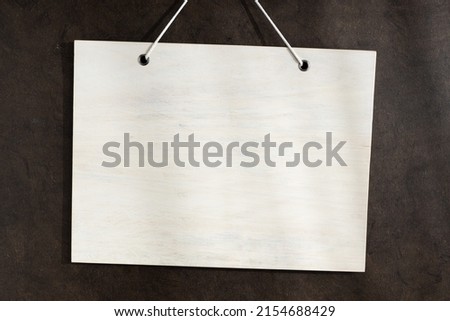 Blank white wooden sign hanging on dark textured wall. Mock up template