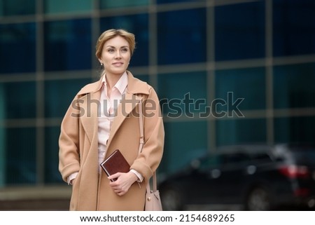 A woman in business clothes and a coat is standing near the business center. Attractive female real estate agent. Freelance theme. Blogger journalist at work.Copy space. High quality photos