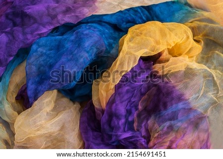 A photo of fabric dyed yellow, blue, purple colors and laid out in an abstract form for use as a background.