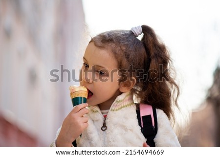 A cute little girl eats ice cream outside. Takeaway. Happiness. Childhood. The concept of delicious food.