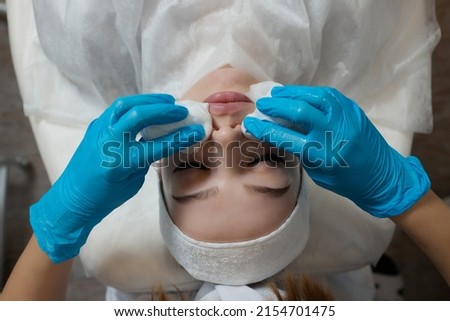 Mirthful young woman lying in a shower cap and hands in rubber gloves cleaning her skin with cotton pads.