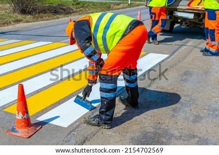 A road worker paints, repairs a pedestrian crossing on an asphalt surface on a city street. Royalty-Free Stock Photo #2154702569