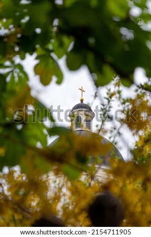 The dome of a Christian Orthodox church is visible through the leaves and flowers of the trees. Beautiful photo of the dome of the church with a cross.