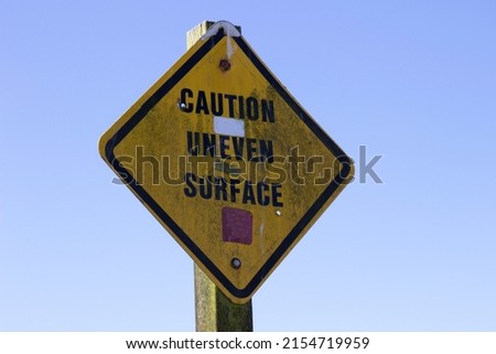 Close up photo of a yellow dirty Caution Uneven Surface sign 