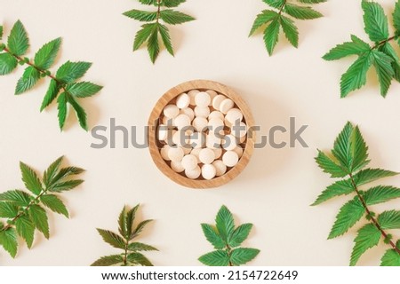 Directly Above Shot Of Pills and green leaves. Tablets in wooden bowl on beige neutral colors background. Homeopathic medicine. Organic medical capsules with herbal plant. Table top view. Copy space. Royalty-Free Stock Photo #2154722649