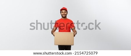 Delivery Concept - Portrait of Happy African American delivery man in red cloth holding a box package. Isolated on Grey studio Background. Copy Space.