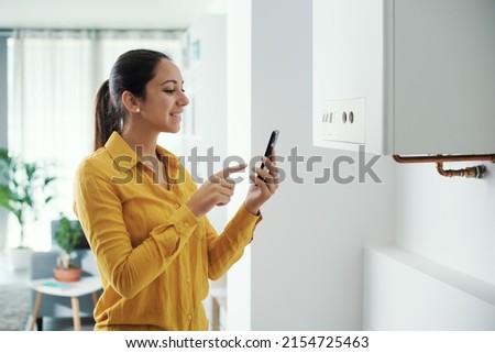 Woman managing and programming her smart boiler using her smartphone, smart home concept Royalty-Free Stock Photo #2154725463
