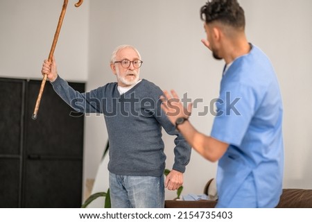 Exasperated pensioner threatening his caretaker with his cane Royalty-Free Stock Photo #2154735403