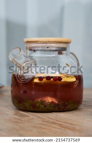 Hot fruit herbal tea poured into transparent cup with hot steam. Fruit herbal tea boiled in clear teapot. Healthy beverage and hot herbal drink concept.                   