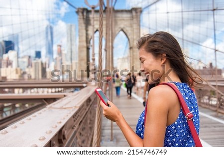 New York tourist woman using phone app walking on Brooklyn Bridge towards Manhattan city skyline. Young female professional multicultural lady, New York City, USA