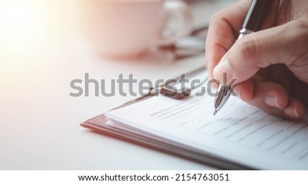 Close-up of Hand using writing pen with questionnaire or paperwork survey question filling in business company personal information form checklist document. Royalty-Free Stock Photo #2154763051