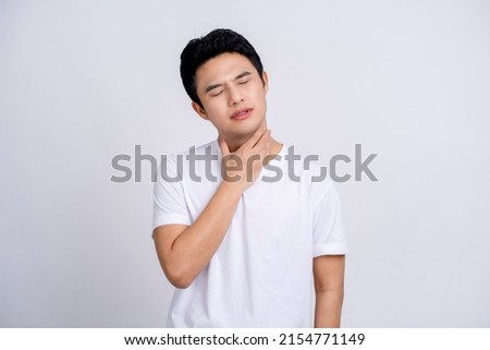 Portrait of young asian man in casual white t-shirt isolated on white background. He had a sore throat and touched his throat. Difficult to swallow. Royalty-Free Stock Photo #2154771149