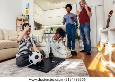 Sad children standing in front of a TV with broken screen holding a ball. Home insurance concept.