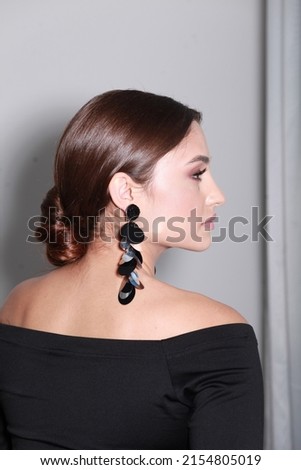 Studio side view image of brunette with professional make up and low glossy bun, wearing statement sequin earrings. Trendy accessorizes and hairstyle.  Elegant looking woman. Minimalist style Royalty-Free Stock Photo #2154805019