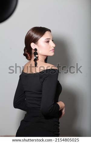 Studio side view image of brunette with professional make up and low glossy bun, wearing statement sequin earrings. Trendy accessorizes and hairstyle.  Elegant looking woman. Minimalist style Royalty-Free Stock Photo #2154805025