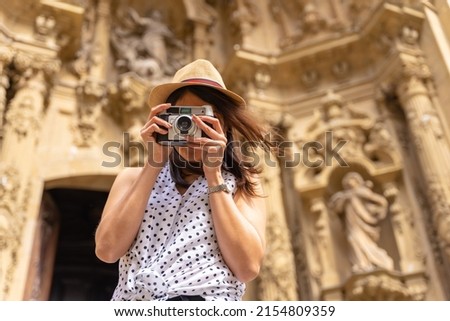 A woman in a hat visiting the city and taking photos with a vintage camera, enjoying summer vacations, concept of female traveler and digital content creator