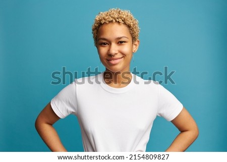 Waist up shot of happy smiling black confident young woman in white t-shirt with blank copy space for your promotional text isolated on blue with hands on waist, wearing nose ring, enjoying good day Royalty-Free Stock Photo #2154809827