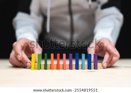 Conceptual photo of hands preparing a row of domino stones.
Domino effect with colored stones and copyspace