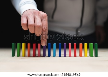 Conceptual photo of a hand picking up a stone from a row of domino stones.
Domino effect with colored stones and copyspace
