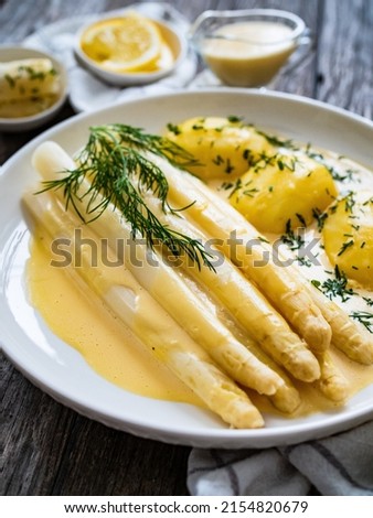  White boiled asparagus in hollandaise sauce with potato puree served on wooden black table  Royalty-Free Stock Photo #2154820679