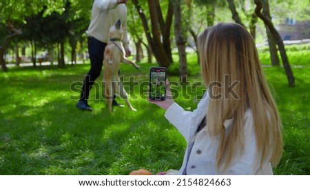 Close-up of a young couple relaxing in the park on a picnic with a dog. A girl takes pictures of her boyfriend playing with a dog on her phone. Picnic in nature