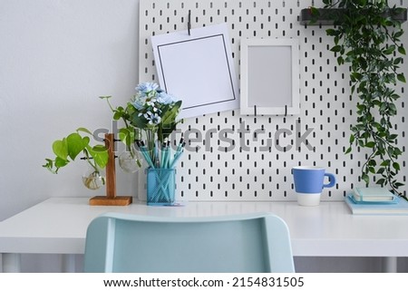 Comfortable workplace with picture frame, houseplant and coffee cup on white table.