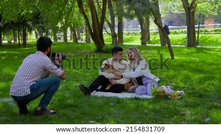 A photographer takes pictures with a camera of a young family with a dog on a picnic. Picnic in nature