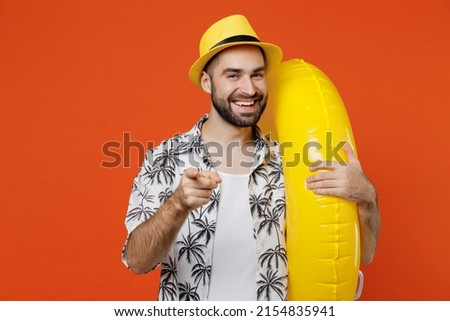 Young smiling tourist man 20s wear beach shirt hat hold inflatable ring point index finger camera on you isolated on plain orange background studio portrait. Summer vacation sea rest sun tan concept Royalty-Free Stock Photo #2154835941