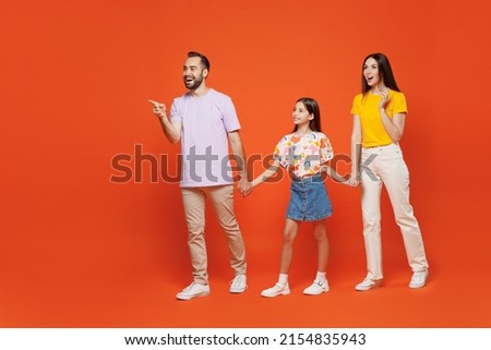 Full body young parents mom dad with child kid daughter teen girl wear basic t-shirts walking go hold hands point finger aside on workspace isolated on yellow background. Family day childhood concept.