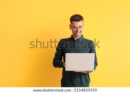 Handsome man in eyeglasses using laptop on yellow background