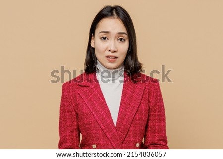 Disappointed displeased sad dissatisfied upset woman of Asian ethnicity wearing red jacket looking camera isolated on plain pastel beige background studio portrait. People lifestyle fashion concept Royalty-Free Stock Photo #2154836057