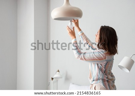 Woman changing light bulb in hanging lamp at home Royalty-Free Stock Photo #2154836165