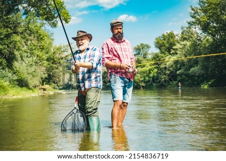 Two men friends fishing. Flyfishing angler makes cast, standing in river water. Old and young fisherman. Royalty-Free Stock Photo #2154836719