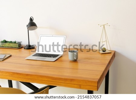 Modern laptop, mobile phone and cup on wooden standing desk near light wall