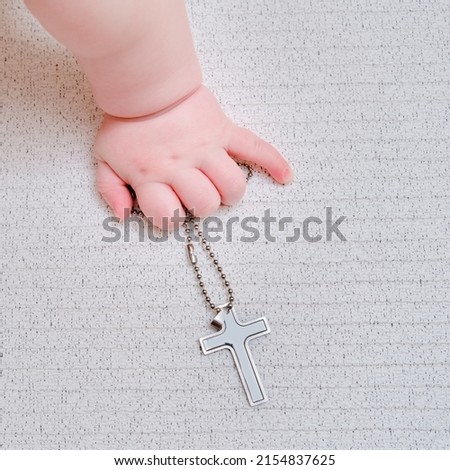 Baby hand and christian religious symbol of the cross, close-up. Children fingers and an object on a white background