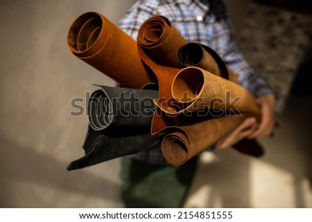 Leather shop. Sale of skin in rolls. Leather workshop. The master tanner holds rolls of leather in his hands. Brown and black genuine leather Royalty-Free Stock Photo #2154851555