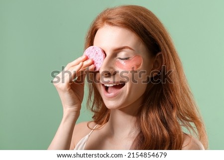 Happy woman with makeup sponge and under eye patches on color background