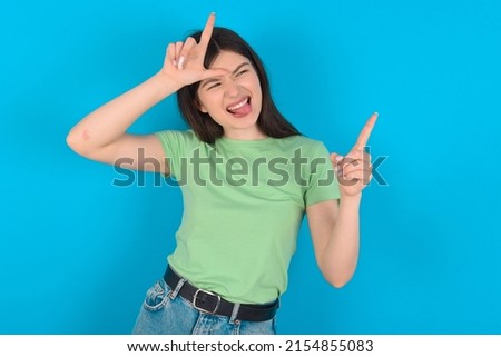 Young caucasian woman wearing green T-shirt over blue background showing loser sign and pointing at empty space